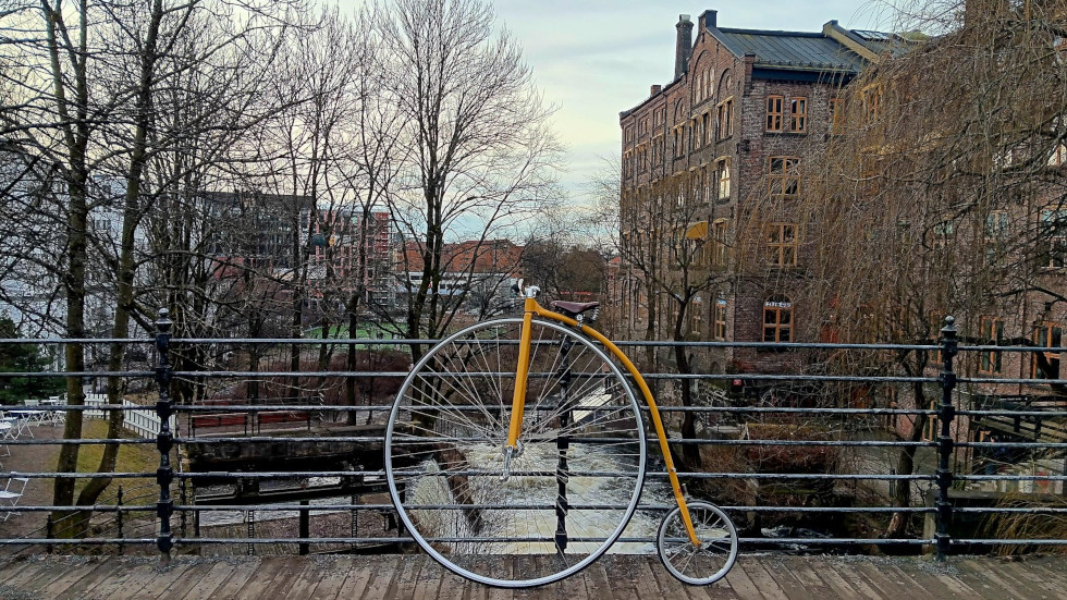 Ordinary bicycle resting on a bridge with a view of a river below and old industrial buildings on the right.