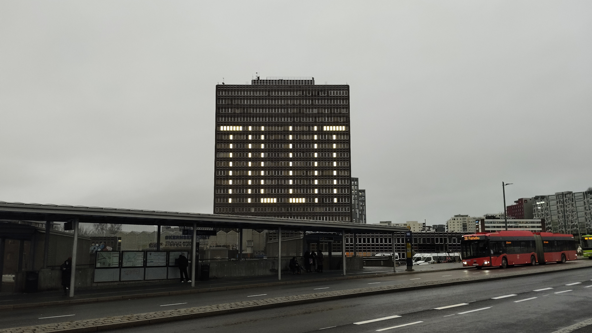 A cloudy urban scene in Oslo featuring a tall office building with illuminated windows spelling out TILLIT.