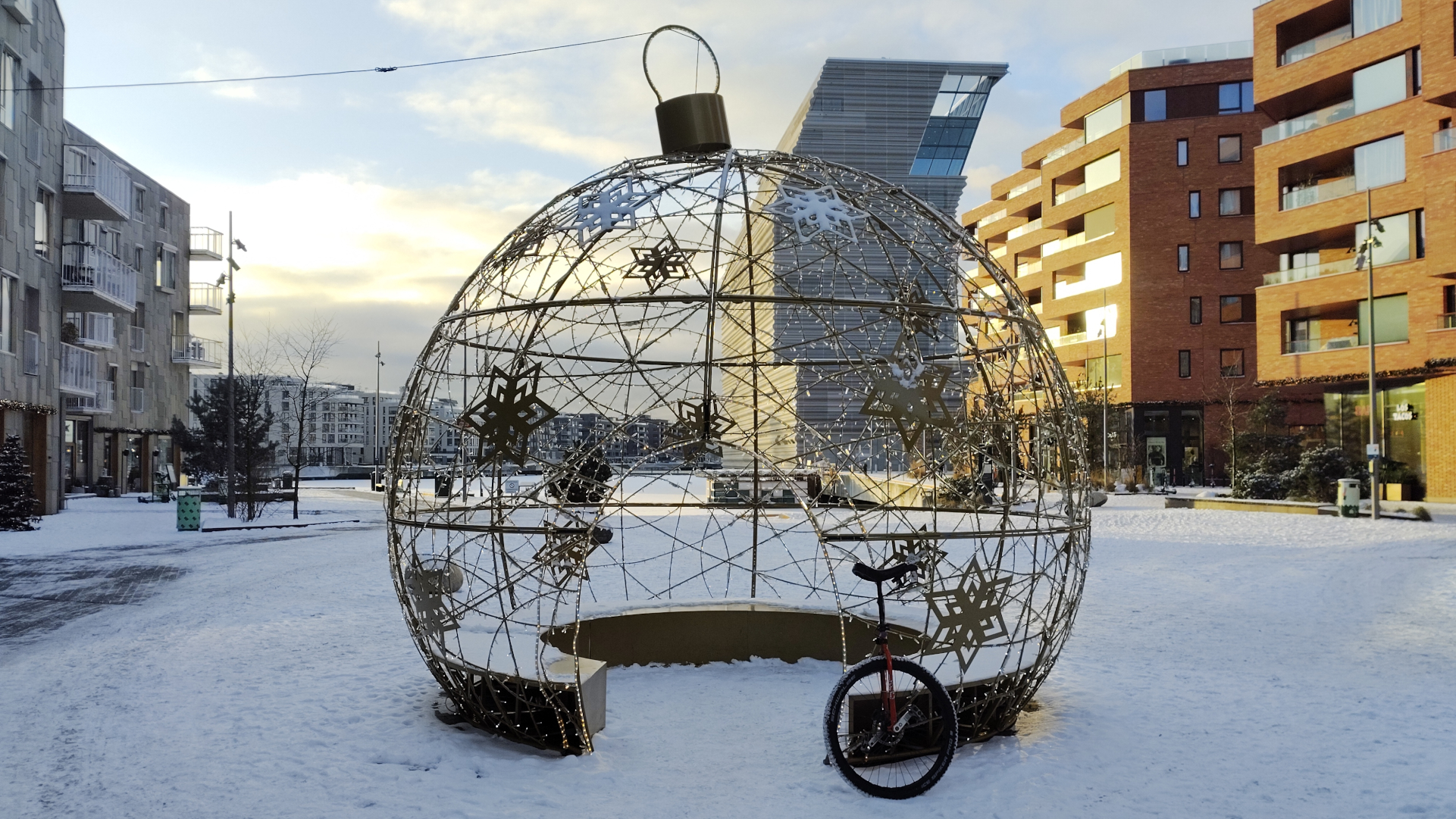 A unicycle leaning on a giant Chritsmas ornament in the snow.