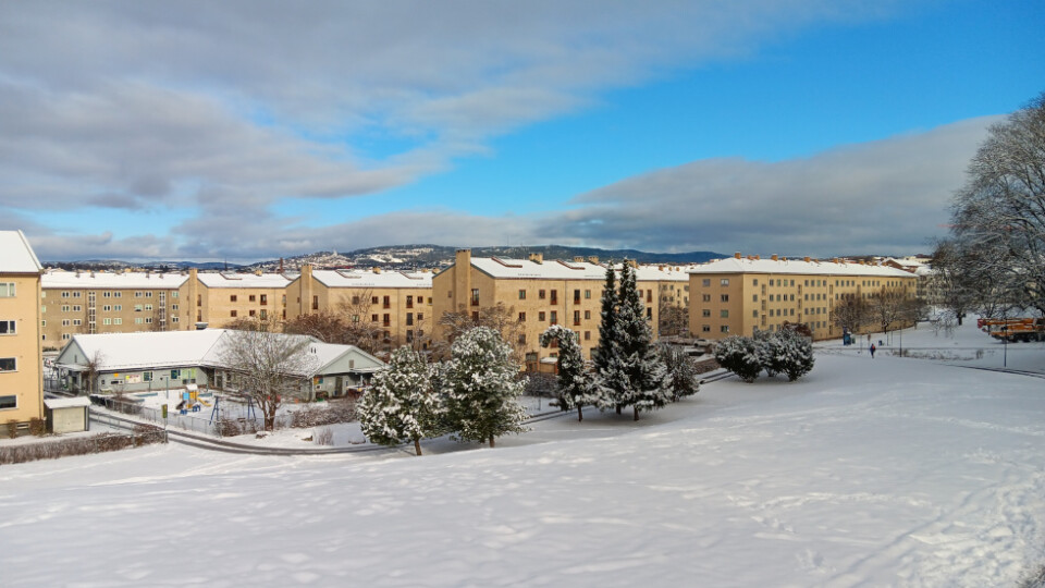 A view looking downhill at some beige residential buildings. There is snow on the ground and a blue sky with some scattered clouds.