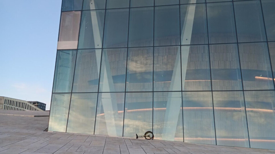 A unicycle resting in front of a large glass window, on a sloped, white stone surface.