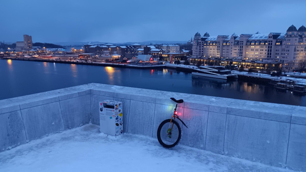 Unicycle leaning against the wall at the top of the Oslo opera house with a view overlooing part of the fjord and some of the city.