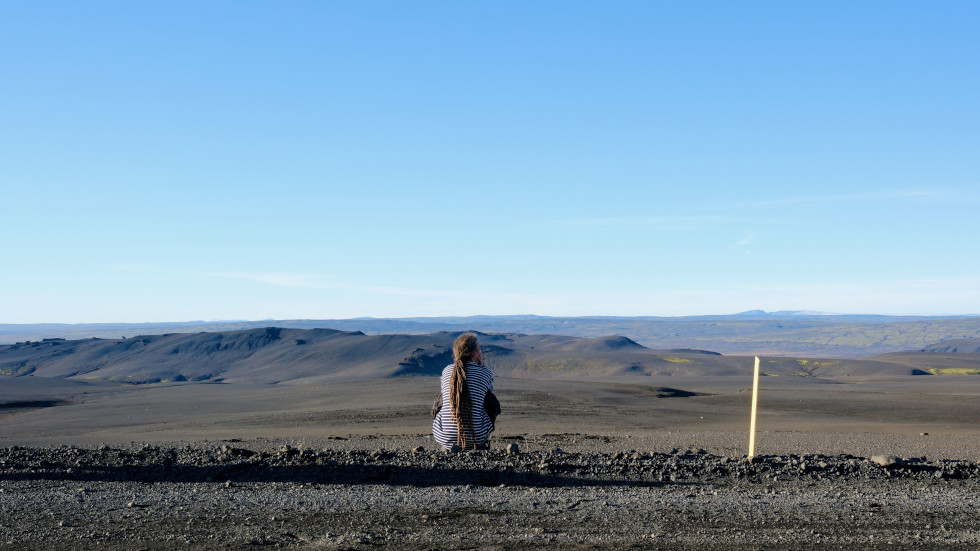 A man, viewed from behind crouched and looking out over the Icelandic landscape
