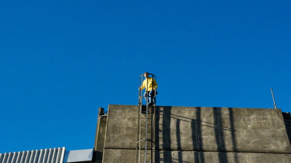 Man with a yellow jacket clicking down an escape ladder of a building
