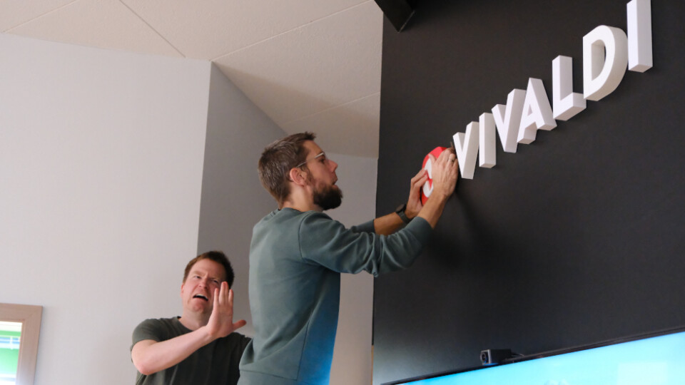 One man putting up a Vivaldi sign on the wall, while another makes an odd facial expression