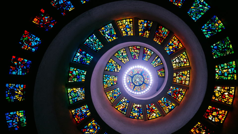 View of a spiral staircase surrounded by stain glass windows.