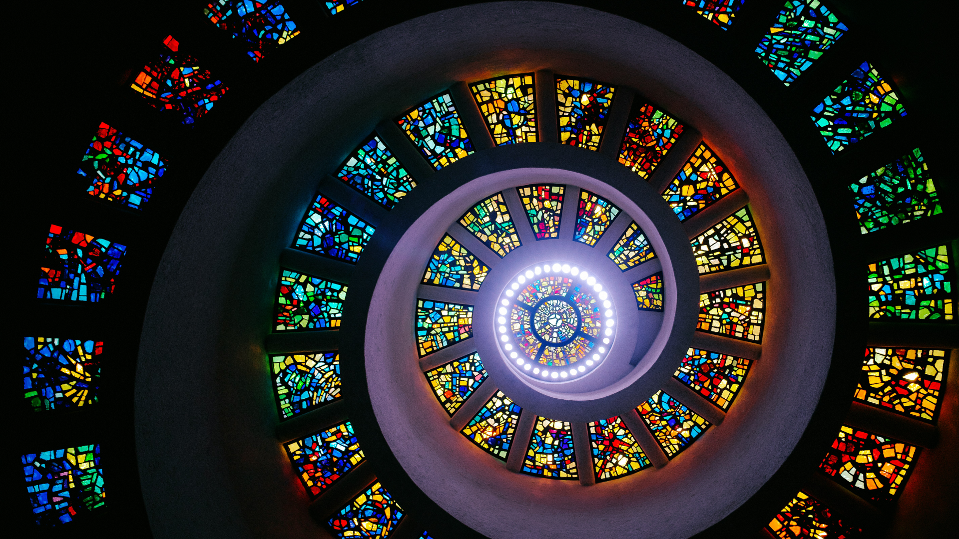 View of a spiral staircase surrounded by stain glass windows.
