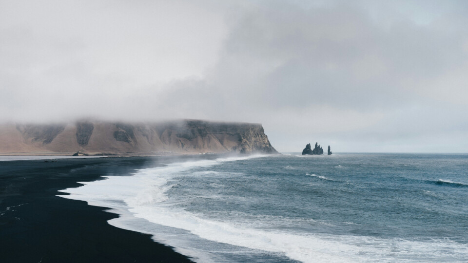 Black‑sand beach with misty cliffs and crashing waves.