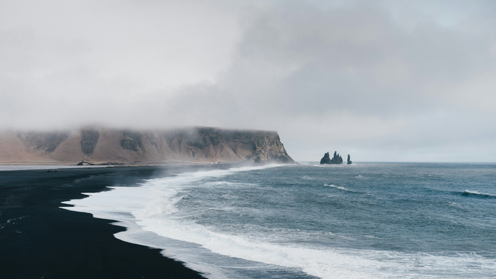 Black‑sand beach with misty cliffs and crashing waves.