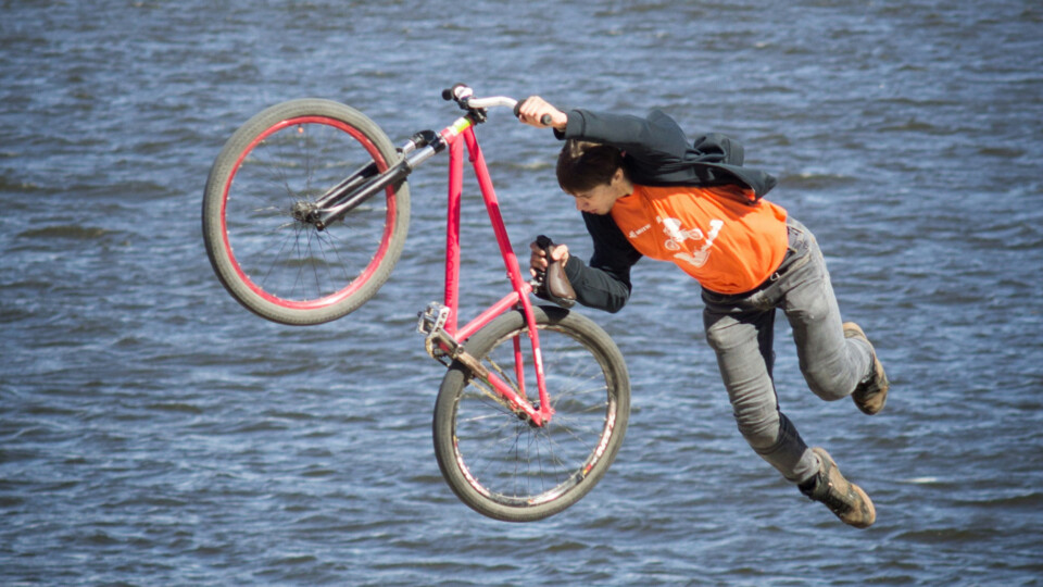 A man leaping into the water holding a bicycle in front of him.