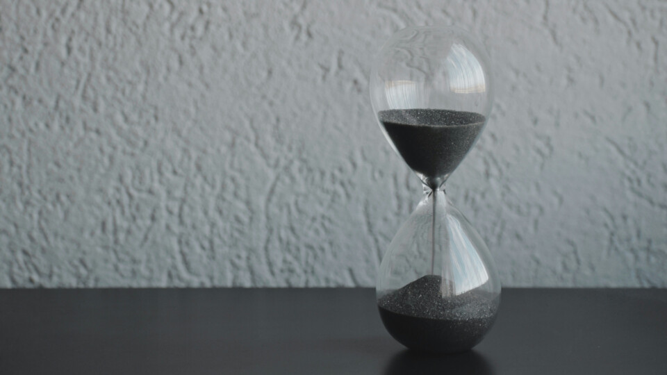 A gray hourglass, with gray sand against a gray backdrop.