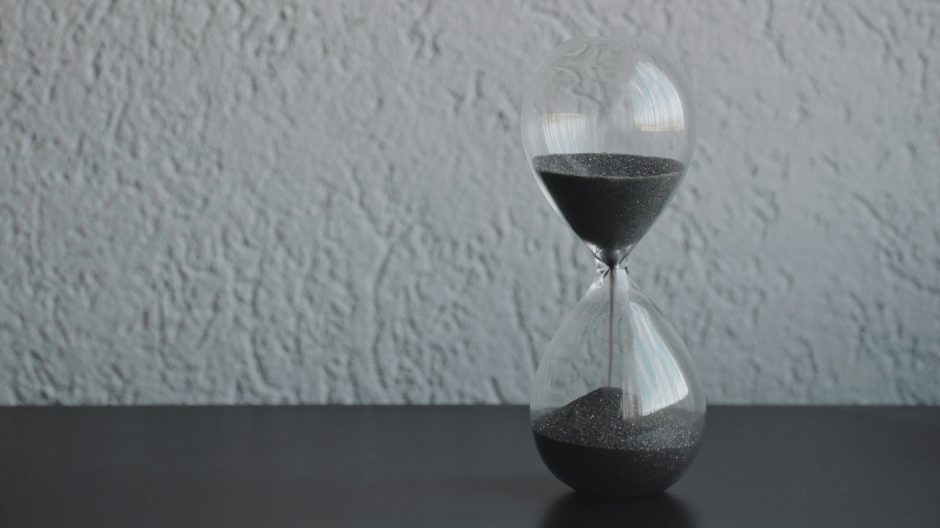 A gray hourglass, with gray sand against a gray backdrop.