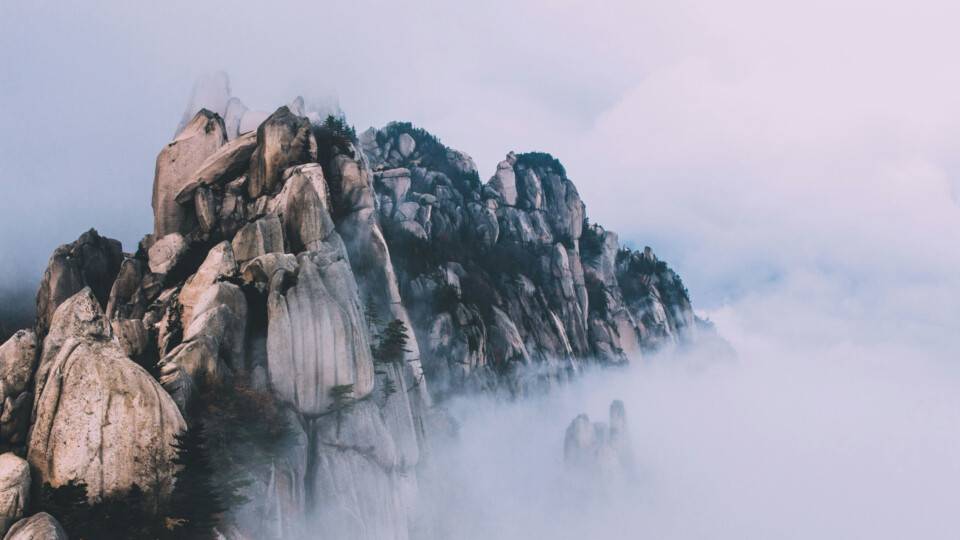 Rugged granite peaks rise through swirling fog and low clouds after rain, revealing a dramatic mountain landscape in South Korea that appears suspended above the cloud layer.