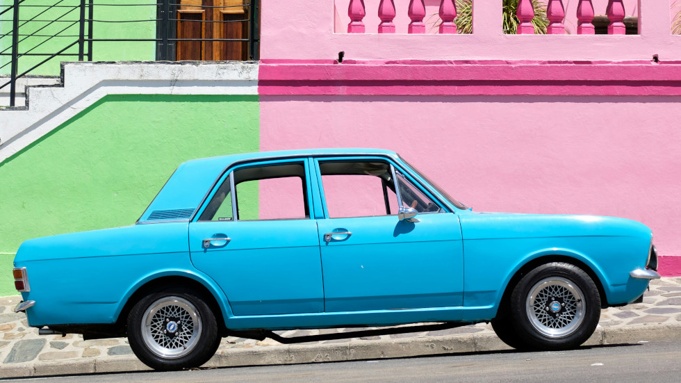 Blue car in front of a pink and green wall