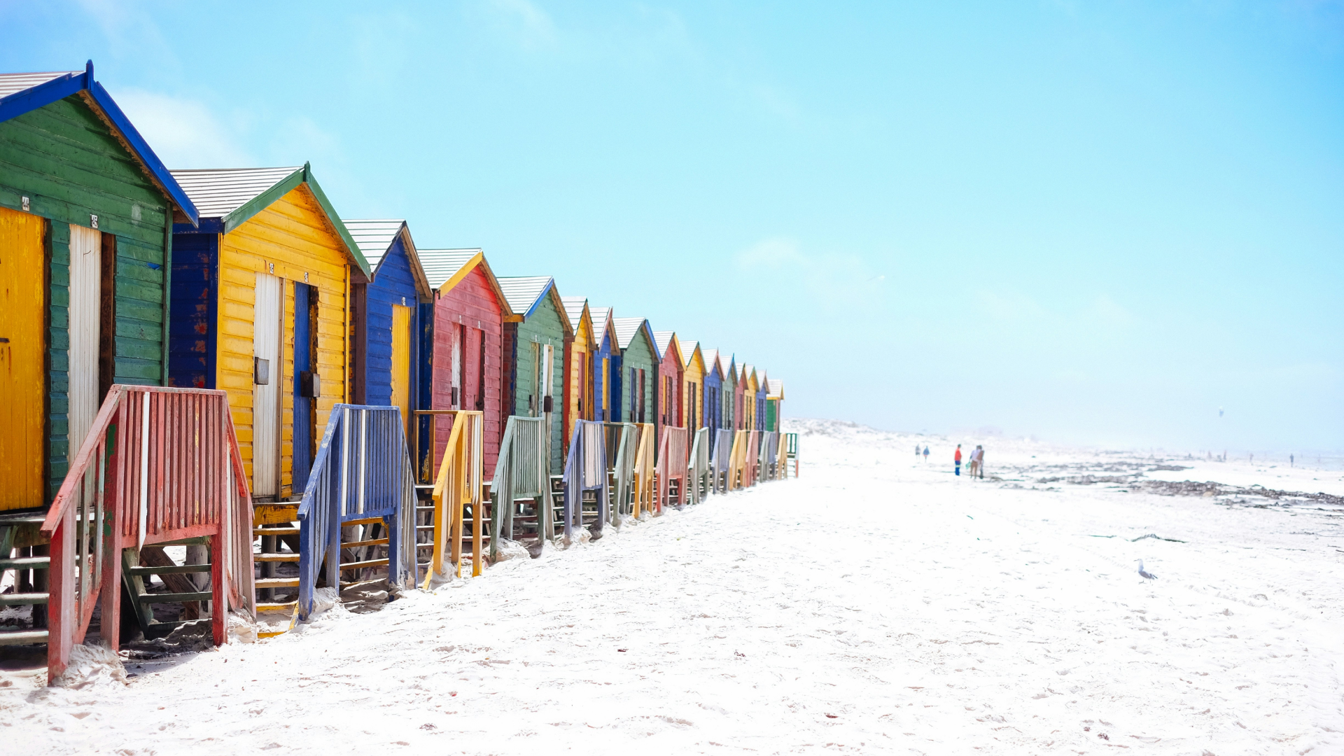 A row of colorful huts on a sandy beach.
