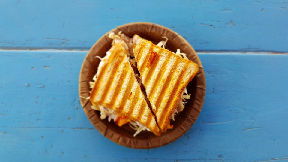 A cheese toastie on a brown plate with a wooden surface, painted blue underneath