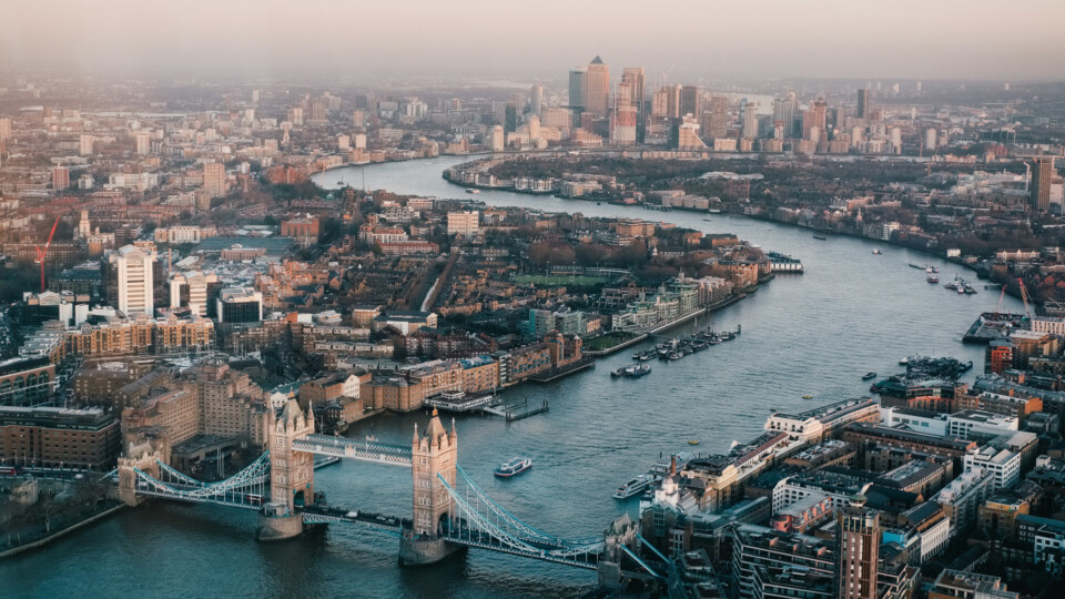 An aerial view of London, Looking down at the winding river Thamas. Tower bridge and the edge of the Tower of London are in the foreground.
