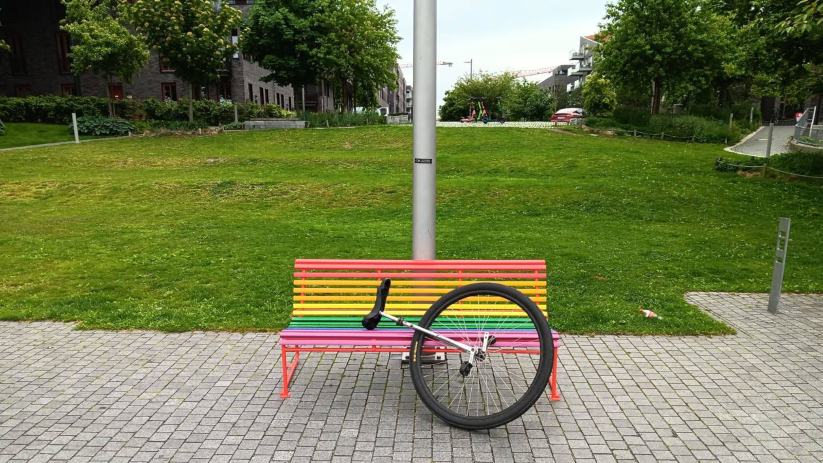 A large wheeled unicycle leaning on a bench painted in rainbow colours.