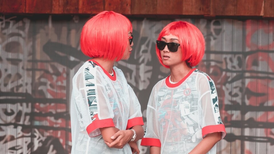 two women with pink hair and sunglasses (with the same outfit) looking at each other