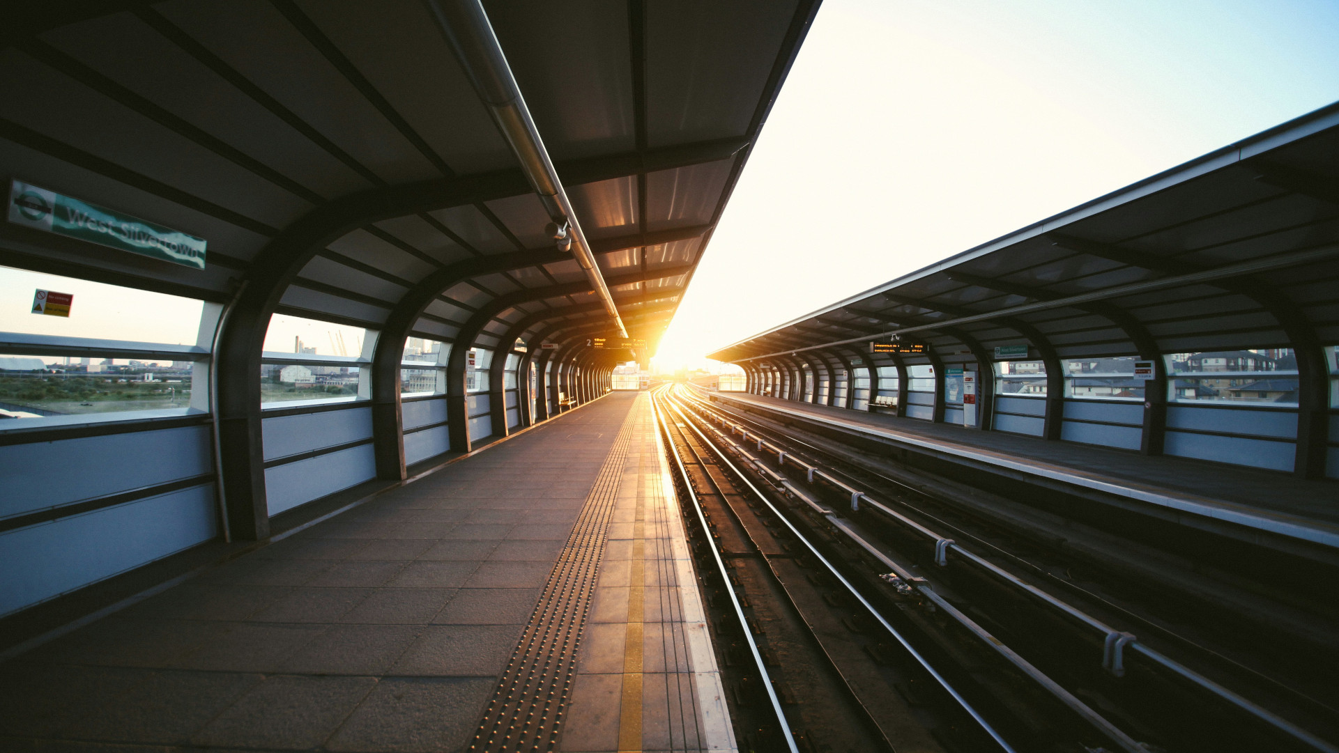 an empty train platform with the sun shinning in the distance.