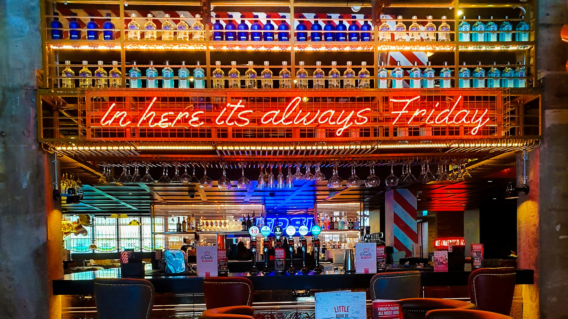 A bar with many bright colors and neon lights, including a neon sign that reads, in here it is always friday