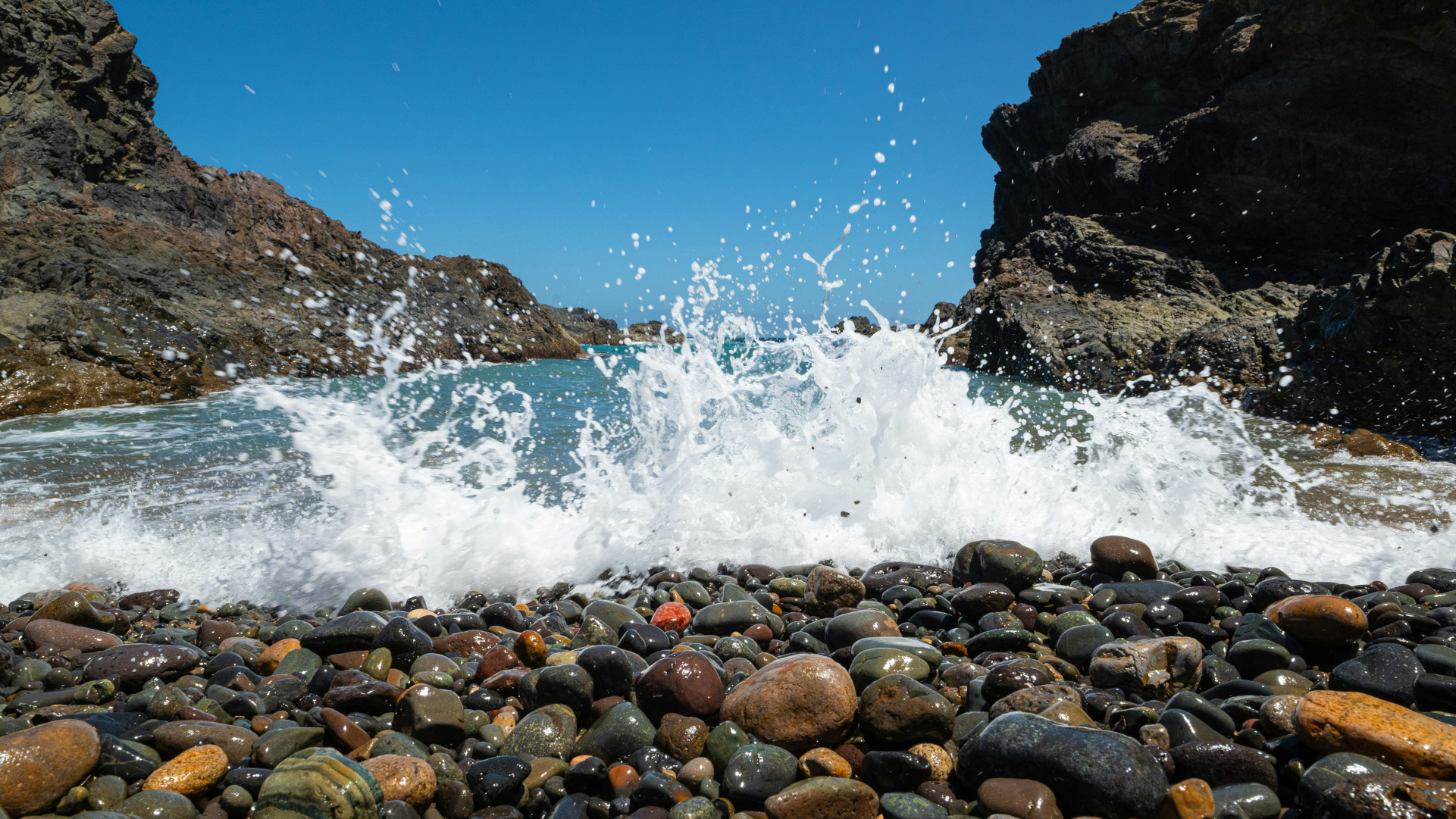 Wave crashing over smooth pebbles between rocky cliffs on the coast of Fuerteventura