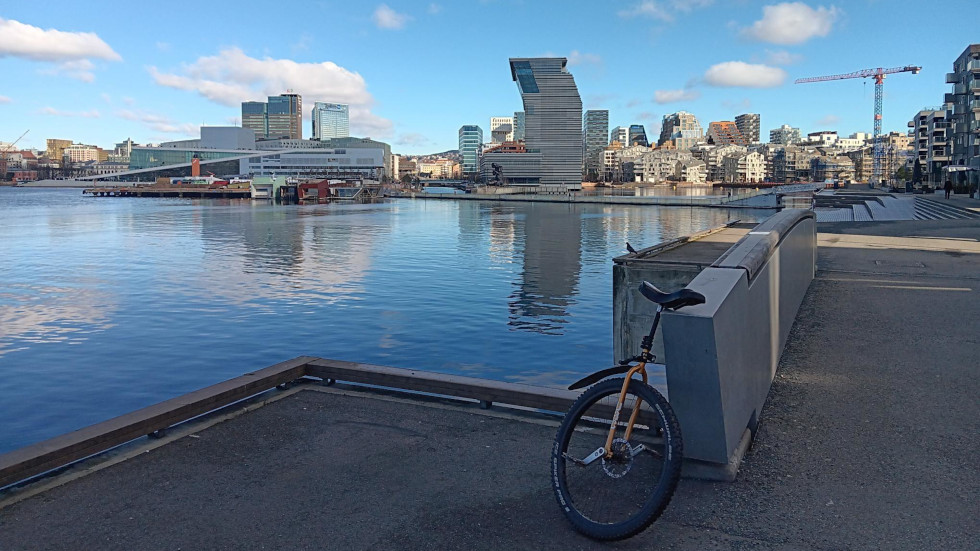 View of Oslo with fjord in the forground and in front of that a unicycle. The sky is blue with scattered clouds.