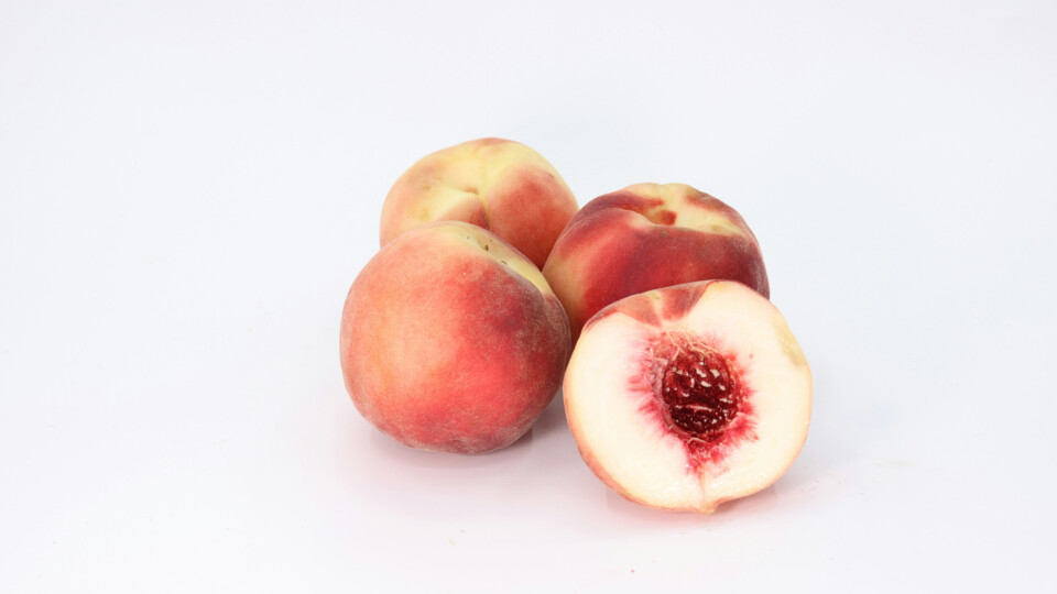 Three and a half peaches. The half is sliced open to expose the stone. On a white background.