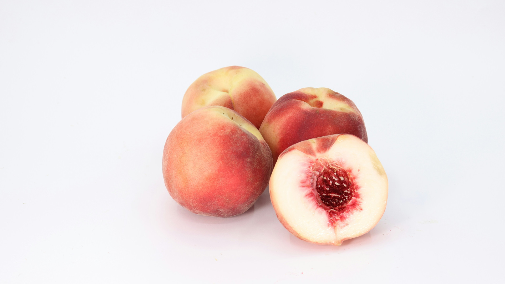 Three and a half peaches. The half is sliced open to expose the stone. On a white background.