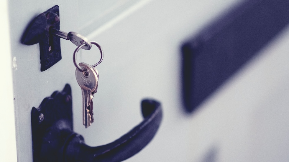 Set of keys hanging out of the lock of a white door with a blue handle
