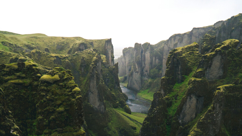 Steep moss covered cliffs with a winding river running through an Icelandic gorge