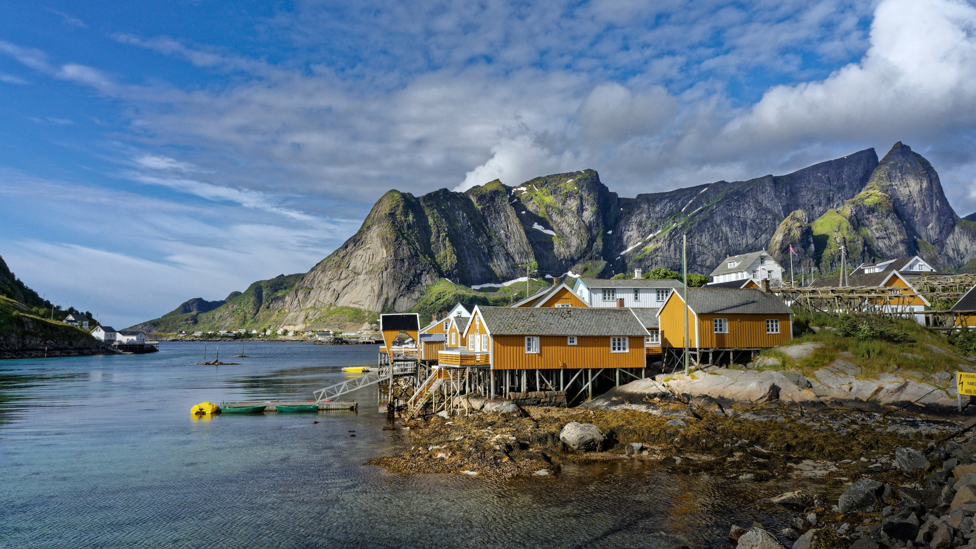 Stilted cabins along the calm Reine shoreline with steep Lofoten mountains rising behind.
