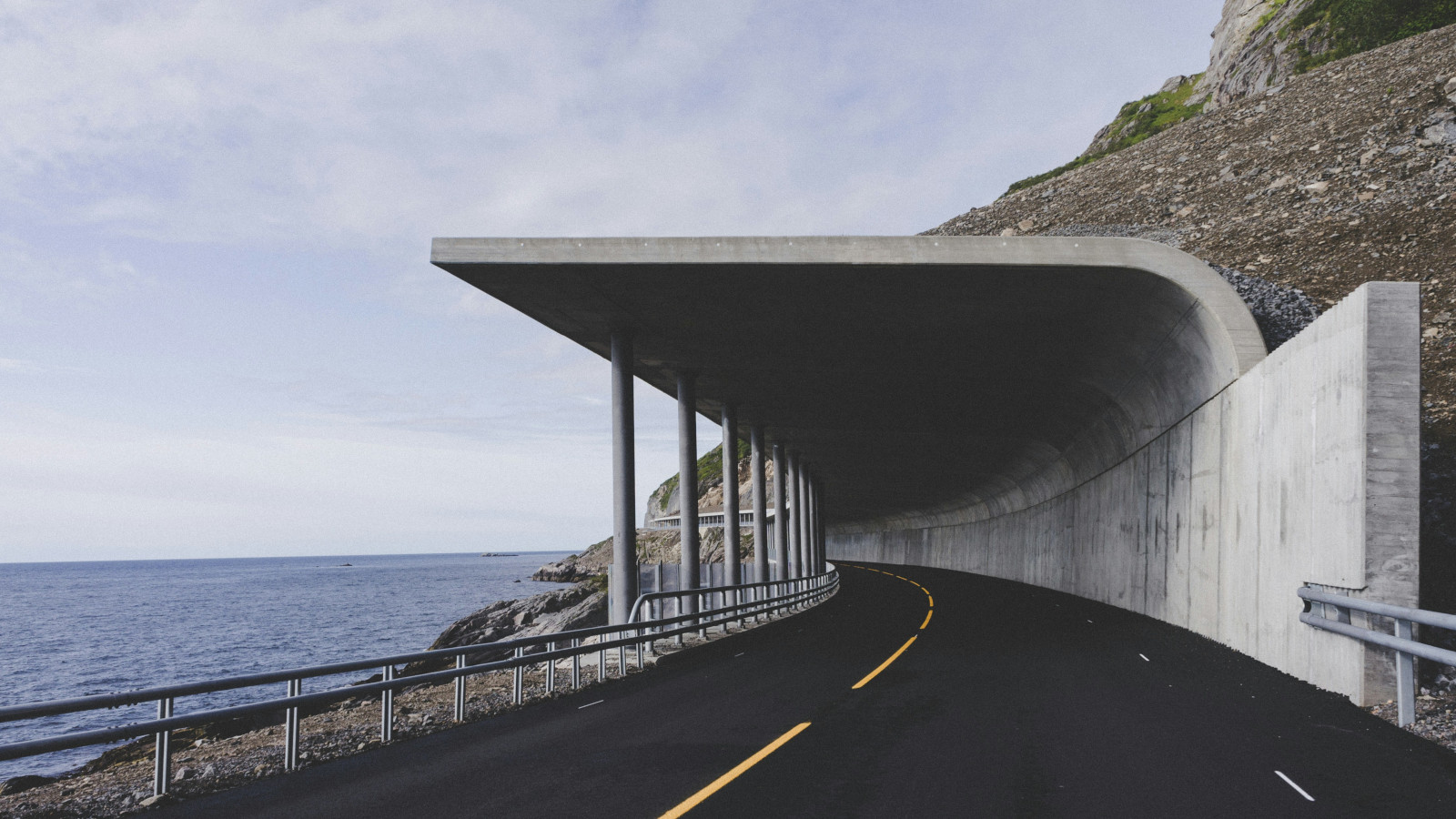 Coastal road with concrete rock‑shield overhang beside the sea.
