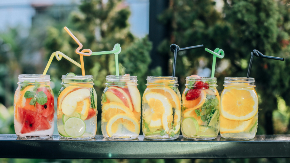 Six clear glass mason jars filled with water and fruit on a black table.
