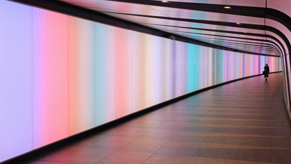 Person walking through a curved, pastel‑lit tunnel in Kings Cross