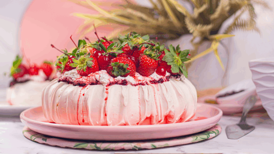 Pink pavlova cake with strawberries on top.