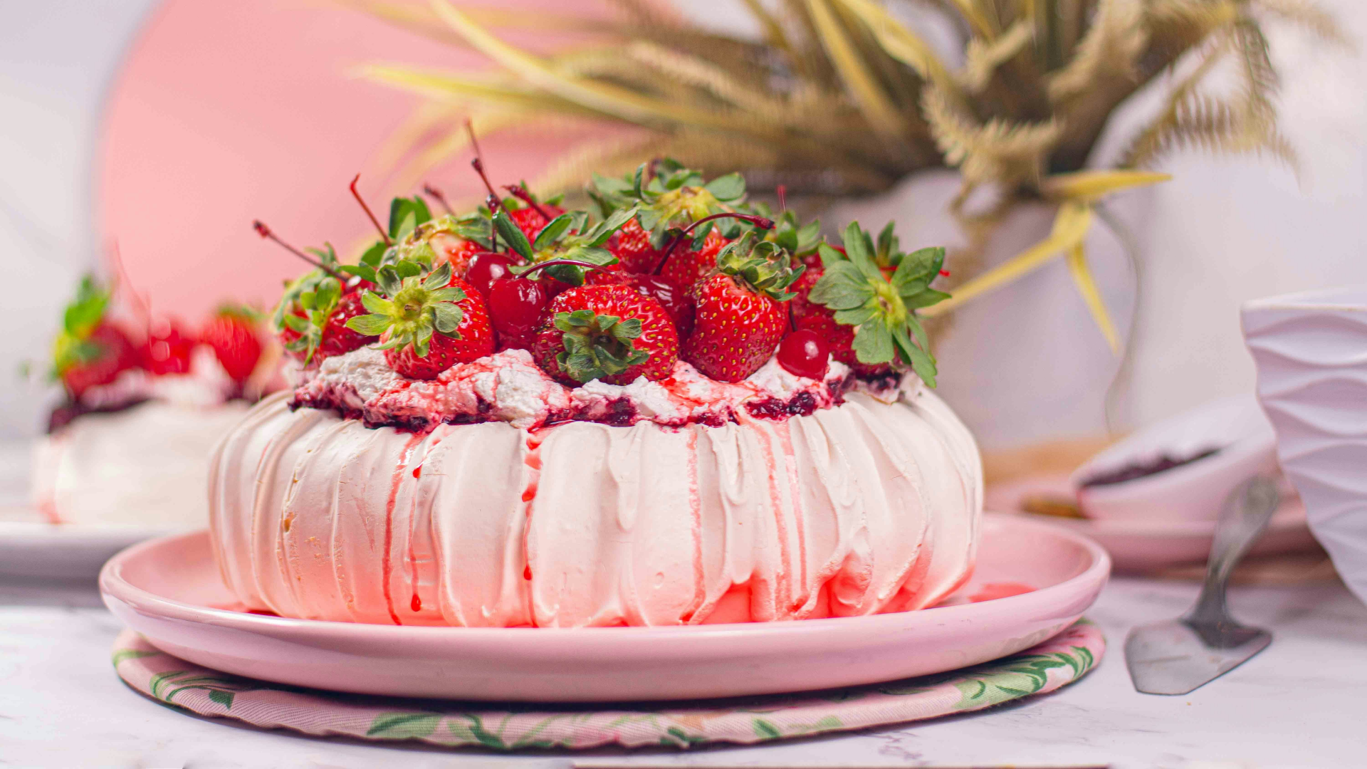 Pink pavlova cake with strawberries on top.