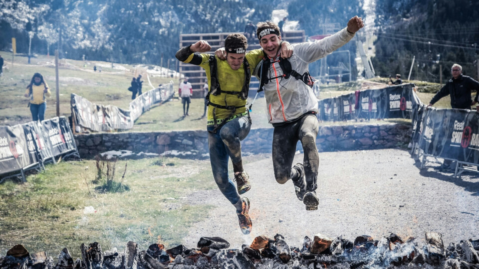 Two athletes jump over burning logs during a Spartan Race.