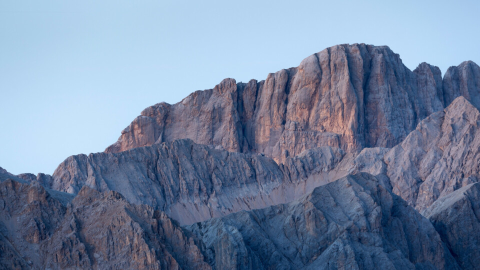 Warm light hitting sharp, layered rocky mountain ridges under a clear sky