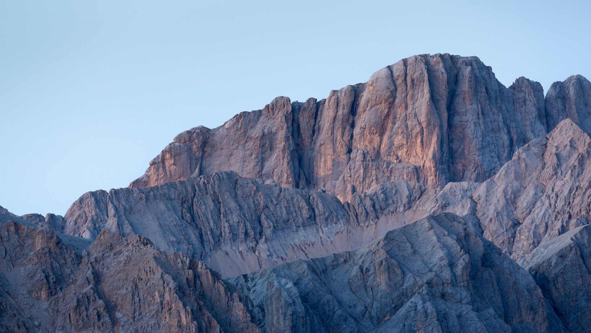 Warm light hitting sharp, layered rocky mountain ridges under a clear sky