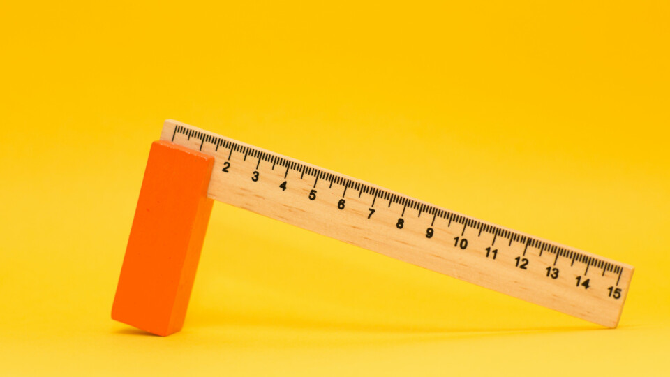 Wooden ruler standing upright on an orange block against a yellow background.