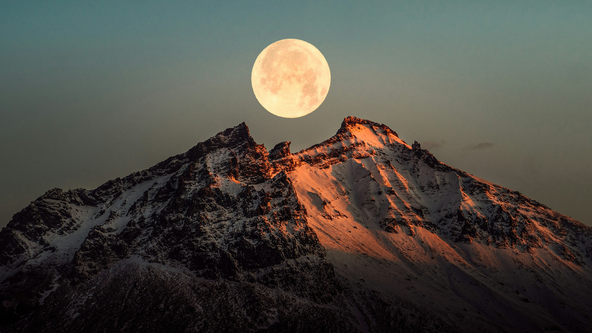 Moon rising over snowy mountain tops.