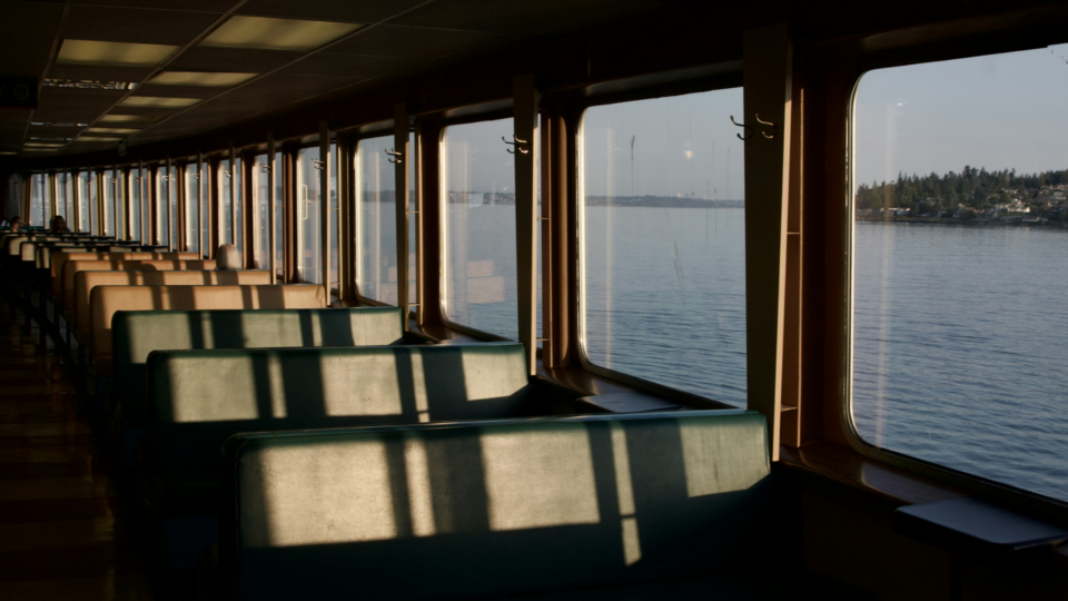 Warm light from a setting sun shining in through ferry windows over the seats.
