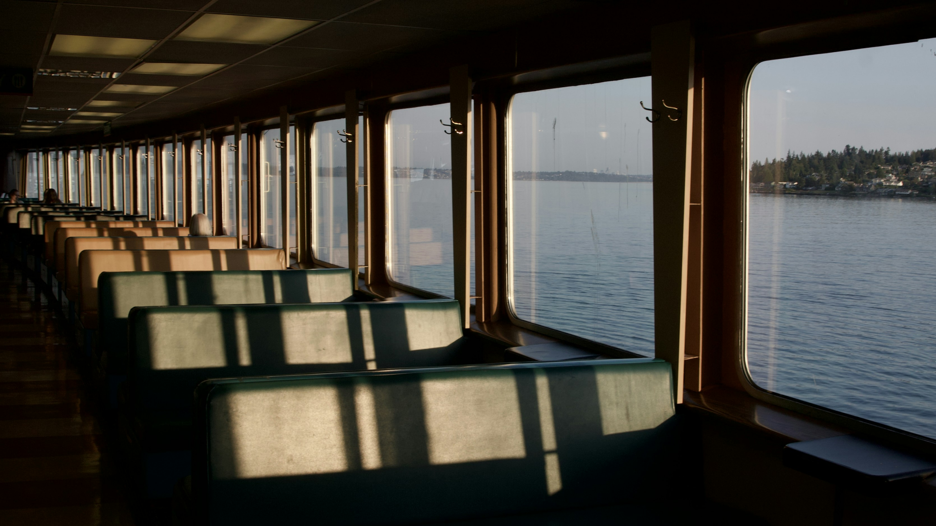 Warm light from a setting sun shining in through ferry windows over the seats.