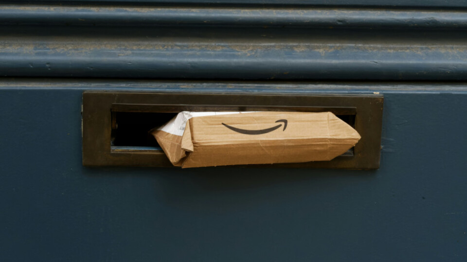A cardbox box rammed halfway through a mailbox that is clearly too small for it. The Amazon smile logo is clearly visible.