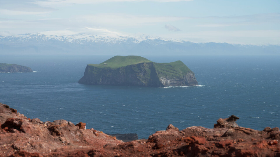 A rocky island with grass on top viewed from a distance across the water.