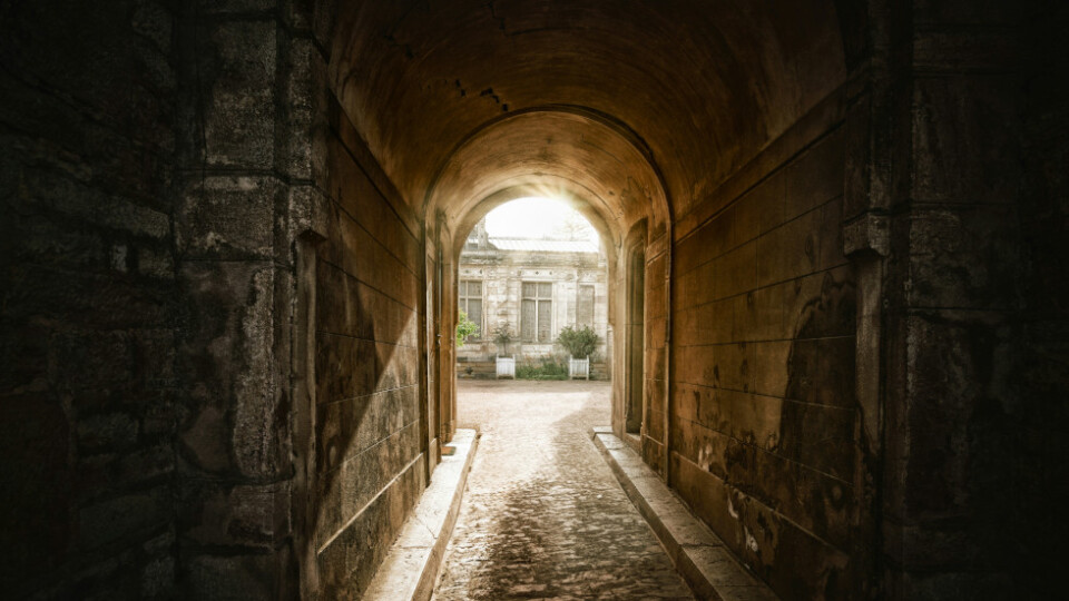 A dark tunnel looking out towards a well lit courtyard