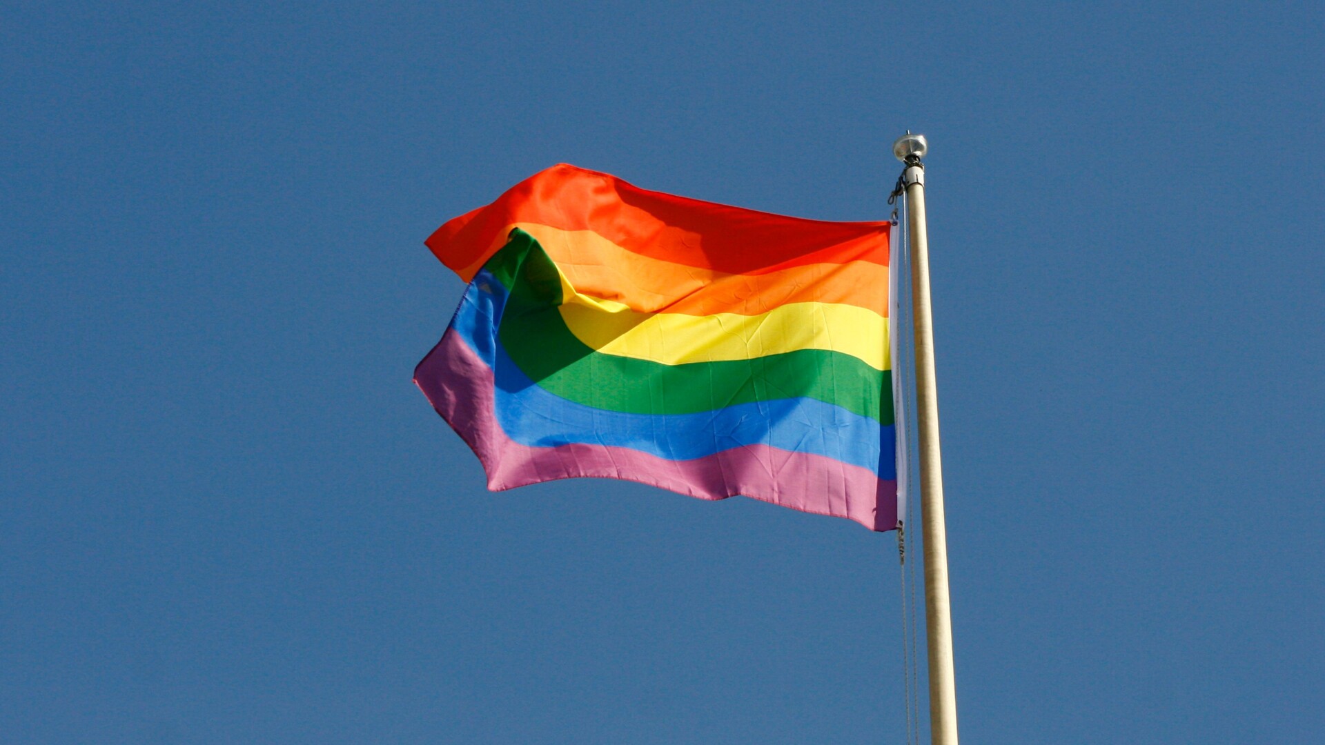 Pride flag waving in the wind with blue sky in the background