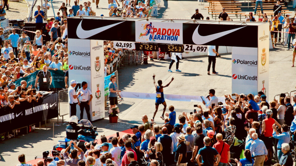 A man running through the finish line of a marathon with his hands in the air.