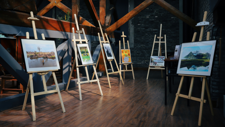 6 easels with paintings on them.